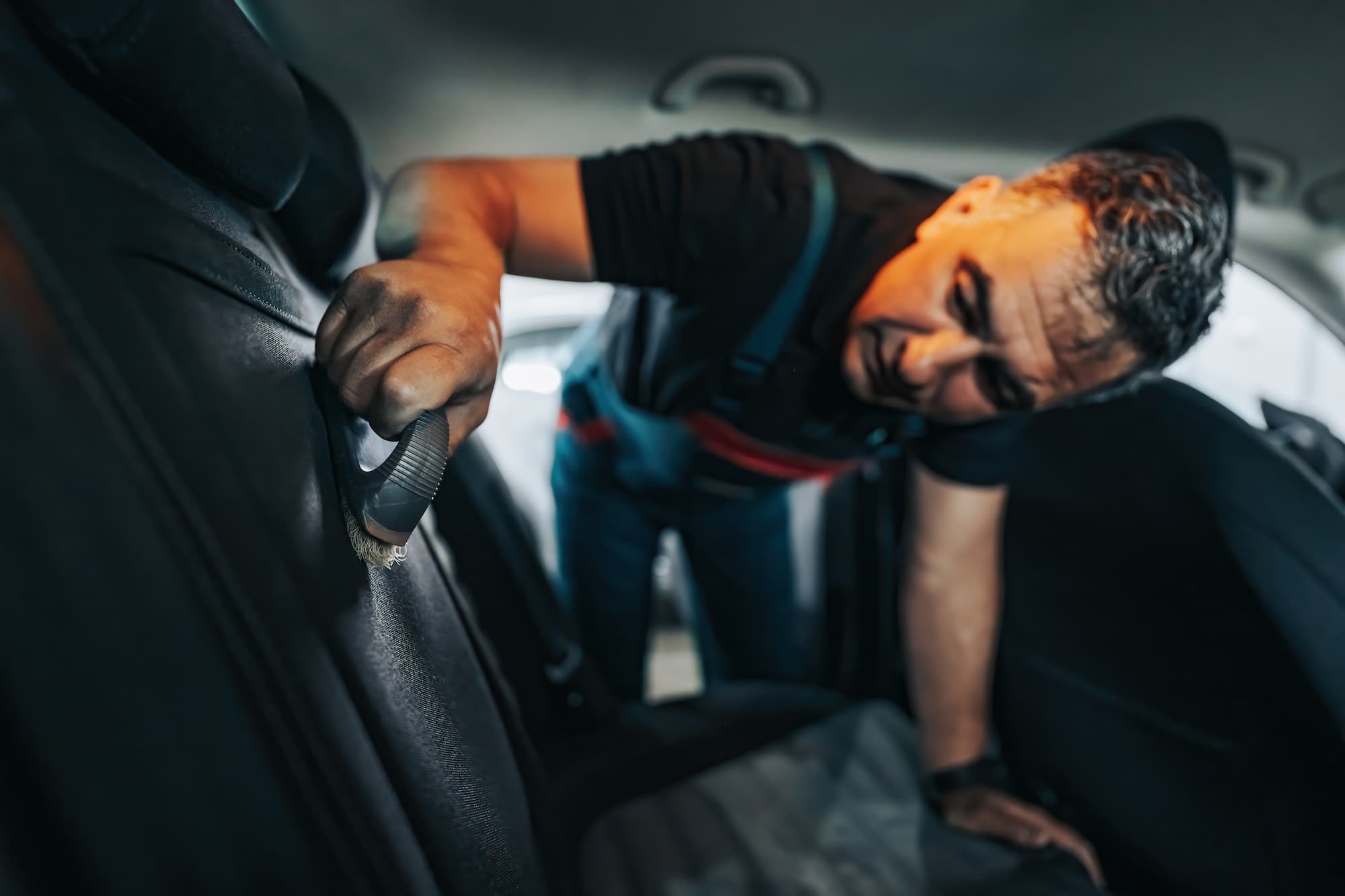 A car wash attendant cleaning the leather seats of a car.